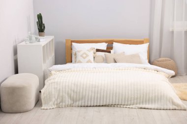 Yatak odasındaki gri duvarın yanında çarşaflı, puflu ve raflı büyük bir yatak. İç tasarım