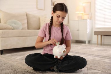 Küçük kız evdeki domuz kumbarasına para yatırıyor. Cep harçlığı ve sorumluluk