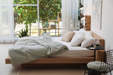 Yatak odasının penceresinin yanında çarşafları ve yastıkları olan rahat büyük bir yatak. İç tasarım