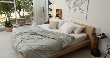 Yatak odasının penceresinin yanında çarşafları, mobilyaları, çiçekleri ve lambası olan rahat büyük bir yatak. İç tasarım