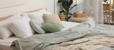 Yatak odasındaki beyaz duvarın yanında çarşafları, çiçekleri ve pufu olan rahat büyük bir yatak.