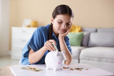 Gülümseyen küçük kız beyaz masadaki kumbaralara para yatırıyor. Cep harçlığı ve sorumluluk