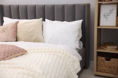 Yatak odasındaki gri duvarın yanında çarşaflı ve raf üniteli büyük bir yatak.