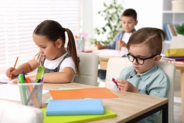 İlkokulda sanat dersi sırasında ahşap masada oturan çocuklar.