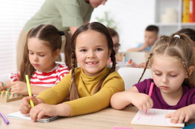 İlkokulda ahşap masada öğretmenden ders alan çocuklar, yakın çekim.