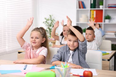 İlkokulda sanat dersi sırasında tahta masalarda el kaldıran sevimli çocuklar.