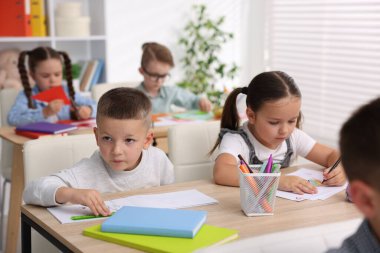 İlkokulda sanat dersi sırasında tahta masalarda oturan sevimli çocuklar.