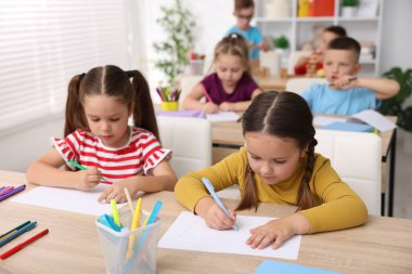 İlkokulda sanat dersi sırasında tahta masalarda oturan çocuklar.