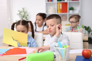 İlkokulda sanat dersi sırasında ahşap masada oturan çocuklar.