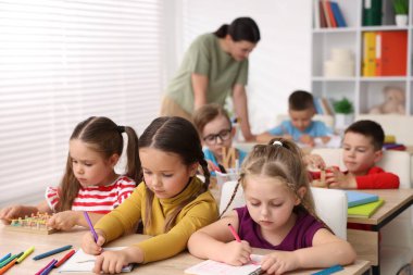 İlkokulda ahşap masalarda öğretmenden ders alan çocuklar.