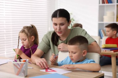 İlkokulda ahşap masalarda öğretmenden ders alan çocuklar.