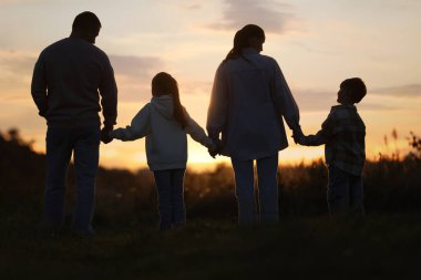 Aile gün batımında, arka planda el ele tutuşuyor.