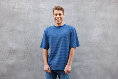 Gri duvarın yanında açık mavi tişört giyen genç bir adam. Tasarım için model