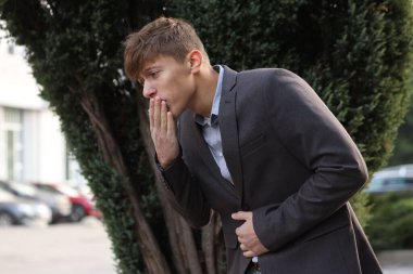 Takım elbiseli genç adam mide ağrısı ve mide bulantısı çekiyor.