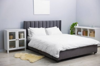 Yatak odasındaki gri duvarın yanında çarşaflı, raf üniteli ve dolaplı büyük bir yatak. İç tasarım