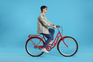 Açık mavi arka planda kırmızı bisiklete binen yakışıklı adam