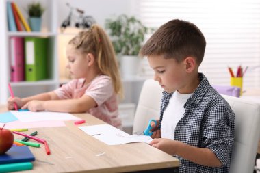 İlkokulda sanat dersi sırasında tahta masada oturan sevimli çocuklar.