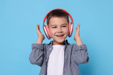 Açık mavi arka planda kablosuz kulaklıklı küçük çocuk.
