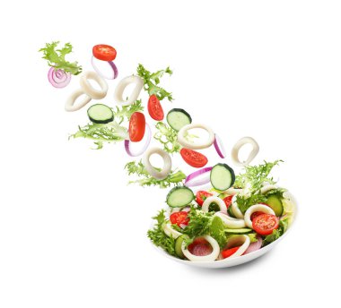 Mürekkep balığı halkaları ve diğer malzemeler beyaz arka planda salata ile kaseye düşüyorlar.