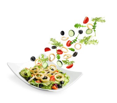 Kalamar halkaları ve diğer malzemeler beyaz arka planda salata ile tabağa dökülüyor.