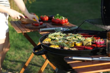 Vejetaryen barbeküsü. Dışarıdaki masada ürünleri kesen kadın, pişmiş sebzelerle ızgaraya odaklan.