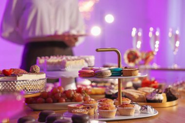 Different delicious desserts on buffet table and waiter, selective focus