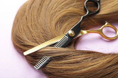 Açık mor arkaplanda güzel kahverengi saç ve makas, yakın plan.