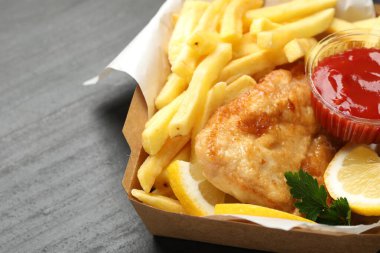 Sos, limon ve maydanozlu İngiliz Geleneksel Balık ve patates kızartması siyah desenli masada, yakın plan.