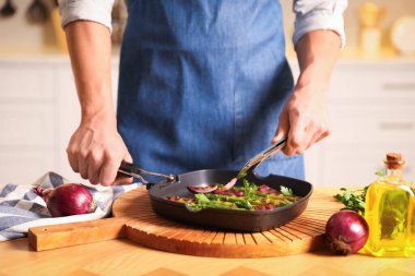 İçerideki masada soğan ve ızgara sebze ekleyen adam, yakın plan.