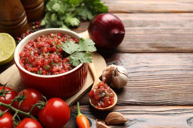 Delicious salsa sauce in bowl and ingredients on wooden table, closeup. Space for text