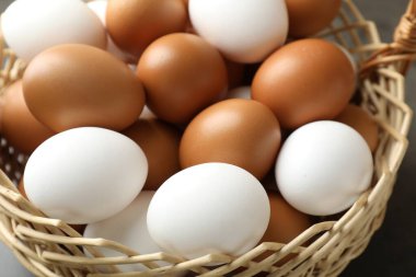 Hasır sepetin içinde çiğ tavuk yumurtası. Gri masada, yakın plan.