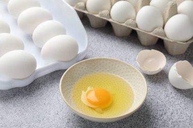 Bir sürü çiğ tavuk yumurtası ve bir tanesi gri masada kırılmış, yakın plan.