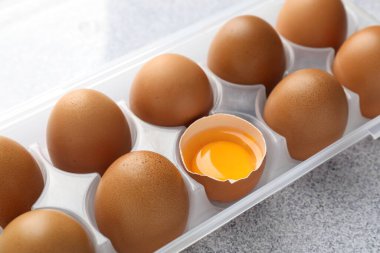 Bir sürü çiğ tavuk yumurtası ve kabın içinde gri masada kırılmış, yakın plan.