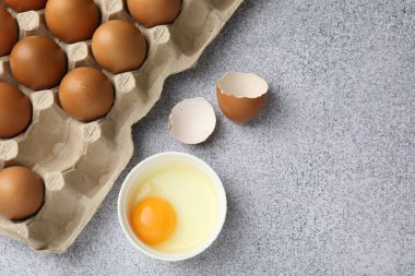 Bir sürü çiğ tavuk yumurtası ve bir tanesi gri masada, düz bir şekilde kasede kırılmış. Metin için boşluk