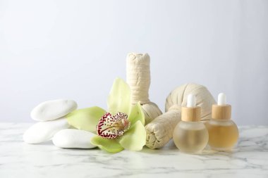 Beyaz mermer sehpanın üzerinde hafif arka planda gerekli yağlar ve bitkisel poşetlerle güzel bir spa kompozisyonu.