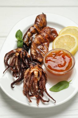 Beyaz ahşap masada limon, sos ve fesleğenle servis edilen lezzetli kalamar.