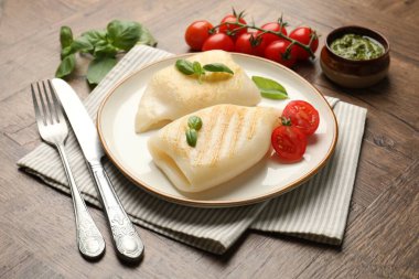 Lezzetli ızgara kalamar, domates, fesleğen ve sos parçaları ahşap masada, yakın plan.