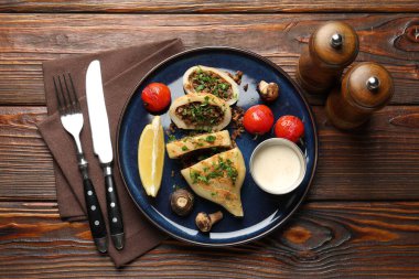 Mantarlı, maydanozlu, domatesli ve soslu ahşap masada servis edilen lezzetli ızgara kalamar parçaları.