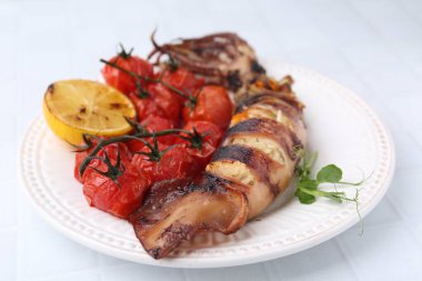 Tasty stuffed squid, microgreens, lemon and tomatoes on white tiled table, closeup