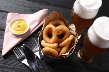 Fried squid rings with sauce and beer served on black wooden table, closeup