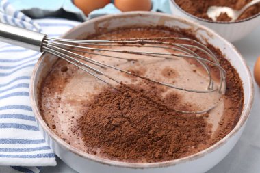 Kakao tozu beyaz fayanslı masada hamurla birlikte kaseye ekleniyor, yakın plan.