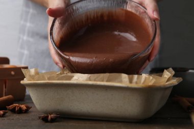 Kadın, ahşap masadaki yemek kabına çikolata hamuru döküyor, yakın plan.