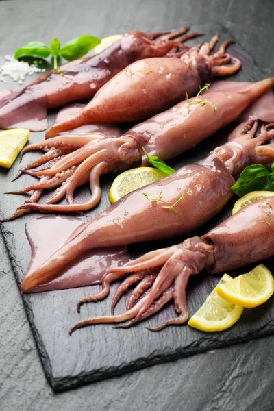 Raw squids, lemon and basil on black table, closeup