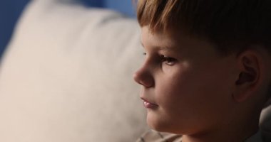 Kanepede oturan üzgün küçük çocuk, yakın plan.