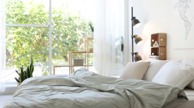 Yatak odasının penceresinin yanında çarşafları, çiçekleri ve lambası olan rahat büyük bir yatak, etrafta hareket eden kamera.