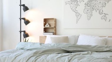 Yatak odasındaki beyaz duvarın yanında çarşafları, sehpası ve lambası olan rahat büyük bir yatak.