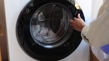 Çamaşır makinesinden çamaşırları çıkaran ve plastik havuza koyan kadın, yakın plan.