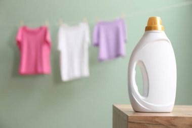 Ahşap masada bir şişe yumuşatıcı ve soluk tozlu yeşil arka planda asılı giysiler, metin için yer