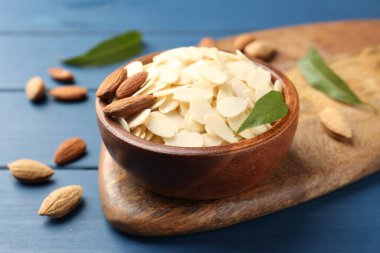 Taze badem taneleri, bütün fındıklar ve yeşil yapraklar mavi ahşap masada, yakın plan.