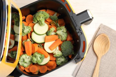 Beyaz ahşap masada çiğ havuç, brokoli ve kabak kızartma makinesi.